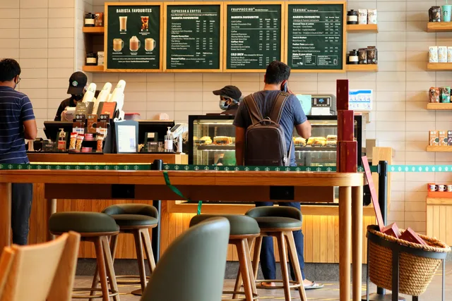 Customers at a bustling coffee shop counter ordering drinks and pastries. Franchisemodellen: krav, kostnader och ansvar